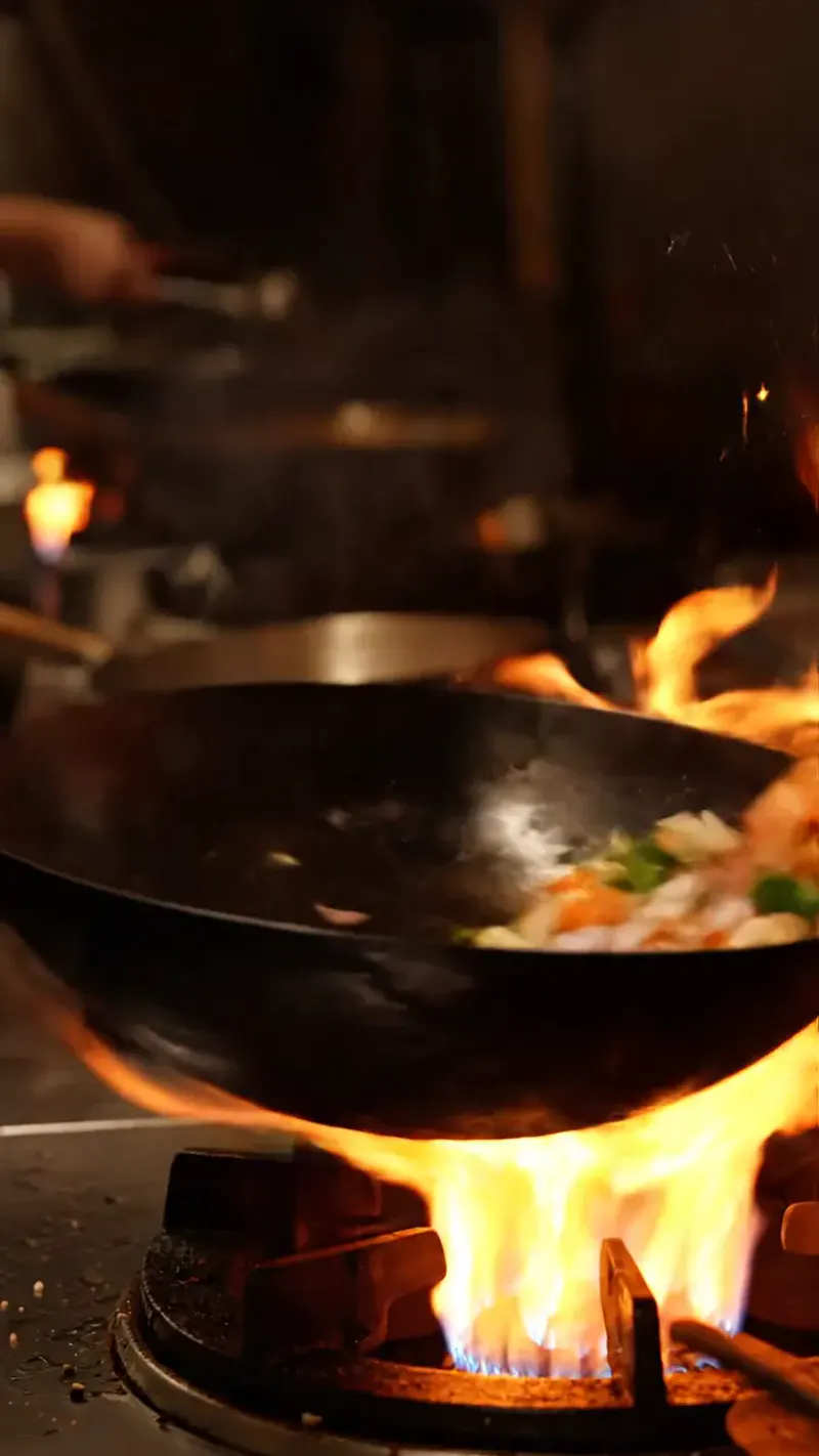 AI-generated vertical video of a chef flipping a pan of vegetables over a roaring flame in a night kitchen, sparks and steam rising — Veo 3.1 Fast, 720p, 4 seconds, 9:16