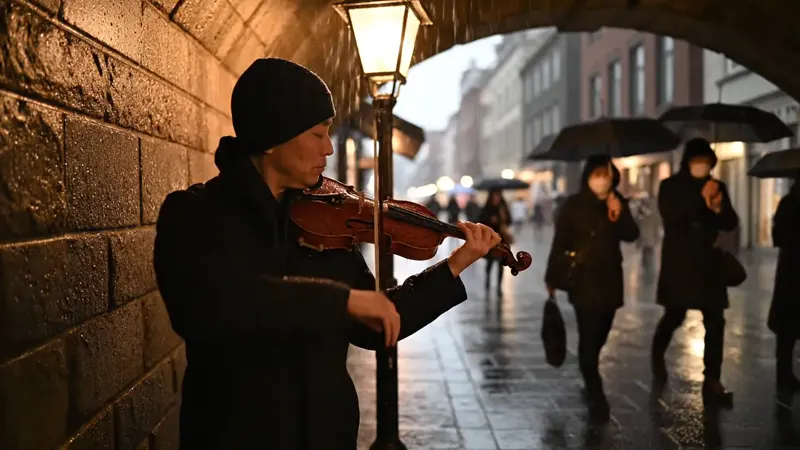 AI-generated video of a street musician playing a violin under a stone archway on a rainy evening, warm lantern light and passers-by with umbrellas — Veo 3.1 Fast, 720p, 4 seconds, 16:9